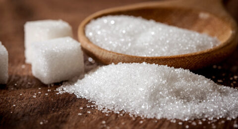 Close up a sugar cubes and cane in wooden spoon on the table